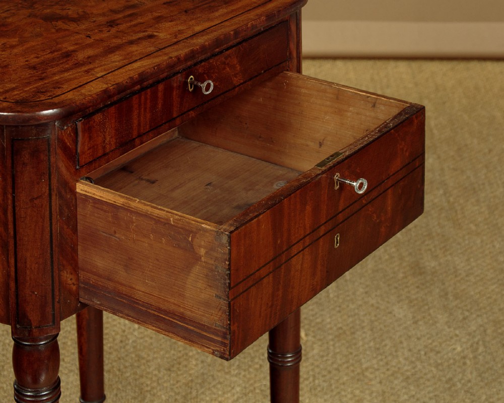 A George III mahogany side table featuring three shallow drawers, ring-turned legs on brass castors, and a rich wood grain finish. View IX