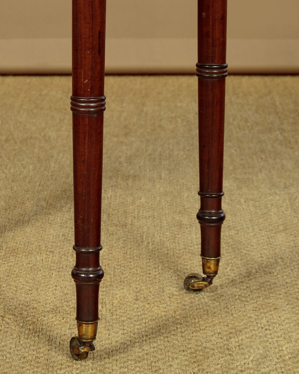 A George III mahogany side table featuring three shallow drawers, ring-turned legs on brass castors, and a rich wood grain finish. View X