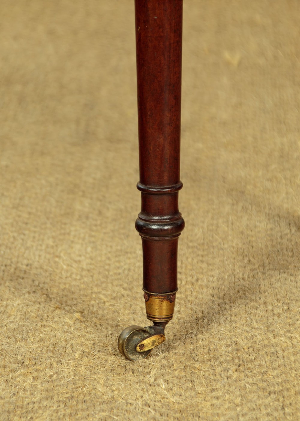 A George III mahogany side table featuring three shallow drawers, ring-turned legs on brass castors, and a rich wood grain finish. View XI