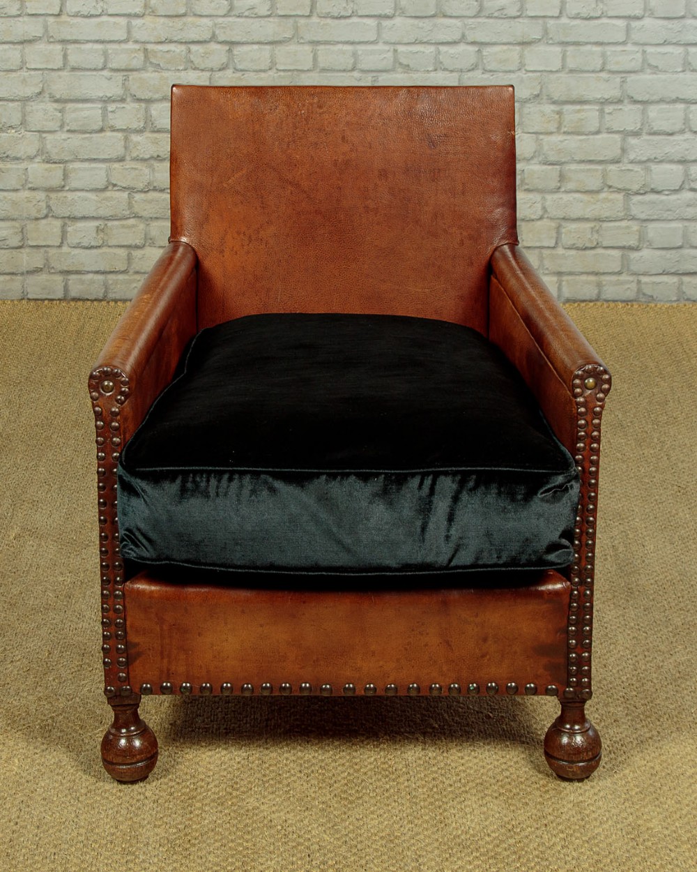 A pair of small 1920s brown leather armchairs featuring brass stud detailing, turned front legs, and dark velvet seat cushions. View IV