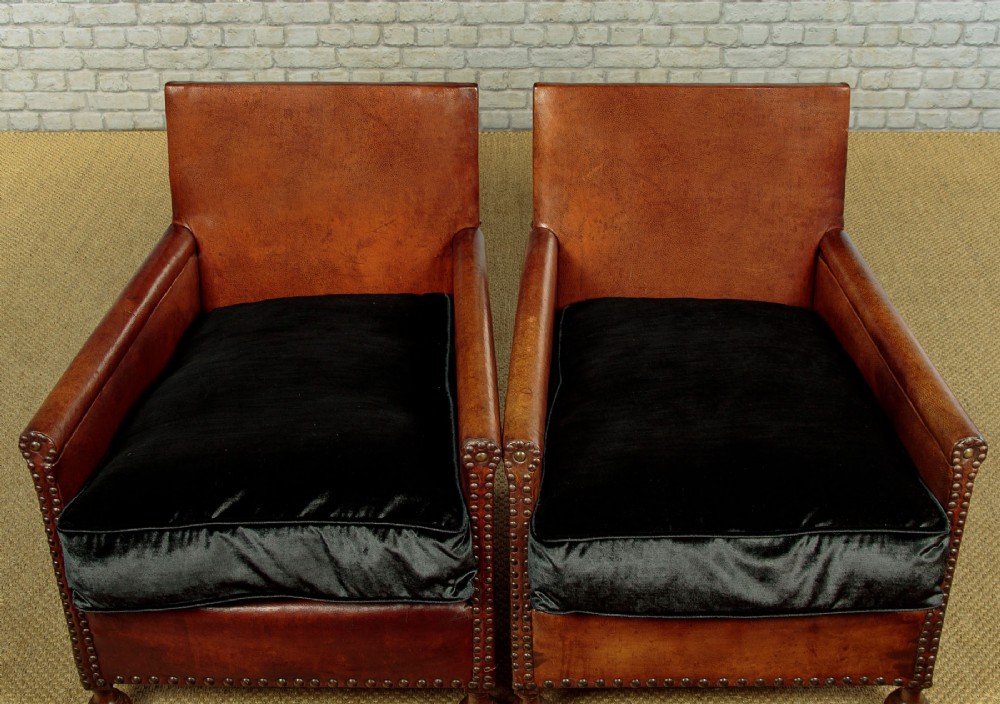 A pair of small 1920s brown leather armchairs featuring brass stud detailing, turned front legs, and dark velvet seat cushions. View VI