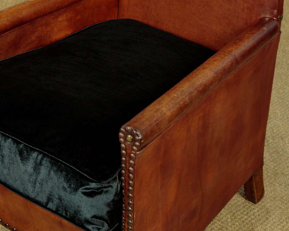 A pair of small 1920s brown leather armchairs featuring brass stud detailing, turned front legs, and dark velvet seat cushions. View IX