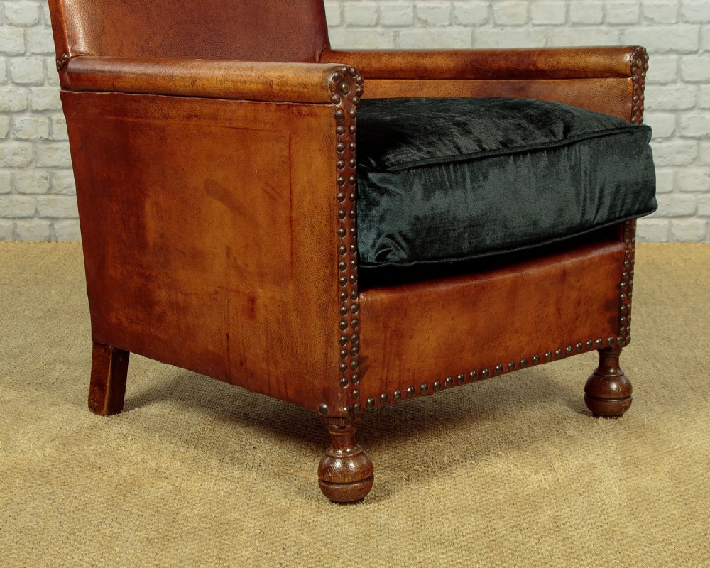 A pair of small 1920s brown leather armchairs featuring brass stud detailing, turned front legs, and dark velvet seat cushions. View XI