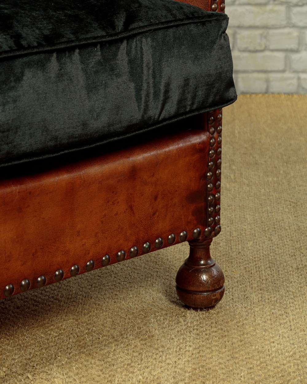 A pair of small 1920s brown leather armchairs featuring brass stud detailing, turned front legs, and dark velvet seat cushions. View XII
