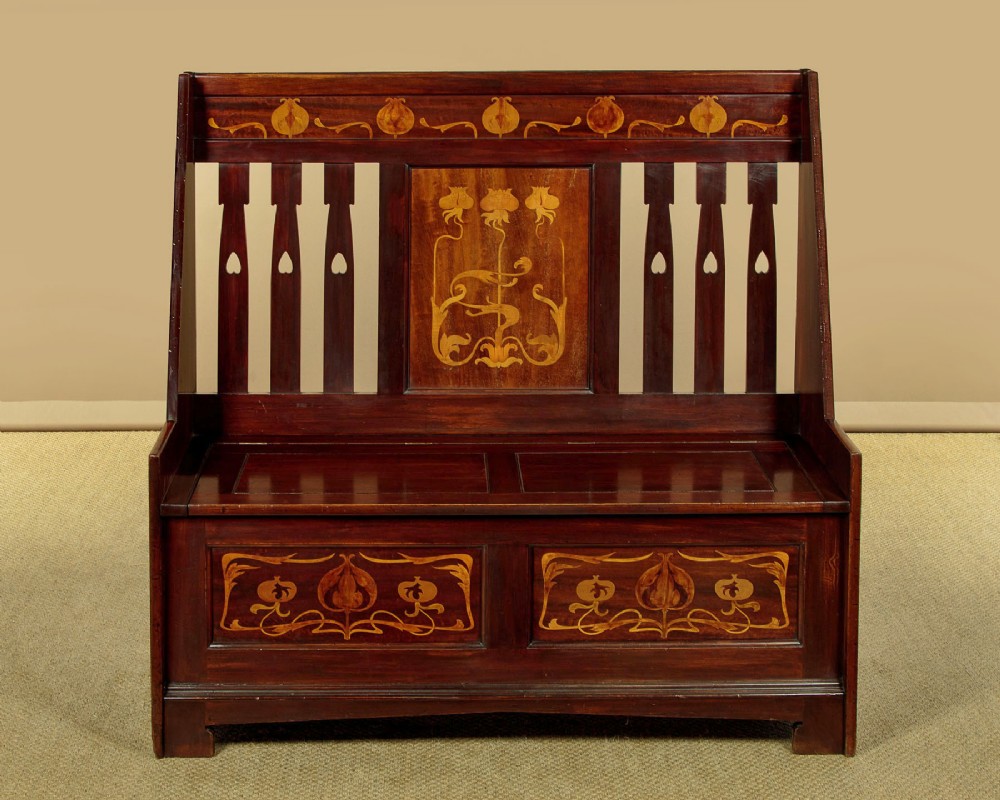 A dark mahogany high-back Arts and Crafts box settle featuring stylised floral marquetry inlay and vertical splat details above a hinged lift-up storage seat. View II
