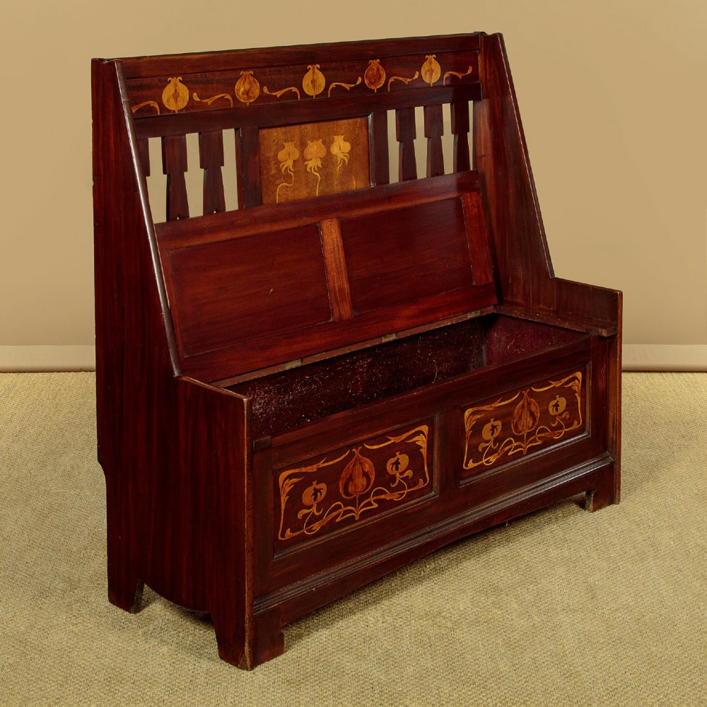 A dark mahogany high-back Arts and Crafts box settle featuring stylised floral marquetry inlay and vertical splat details above a hinged lift-up storage seat. View III