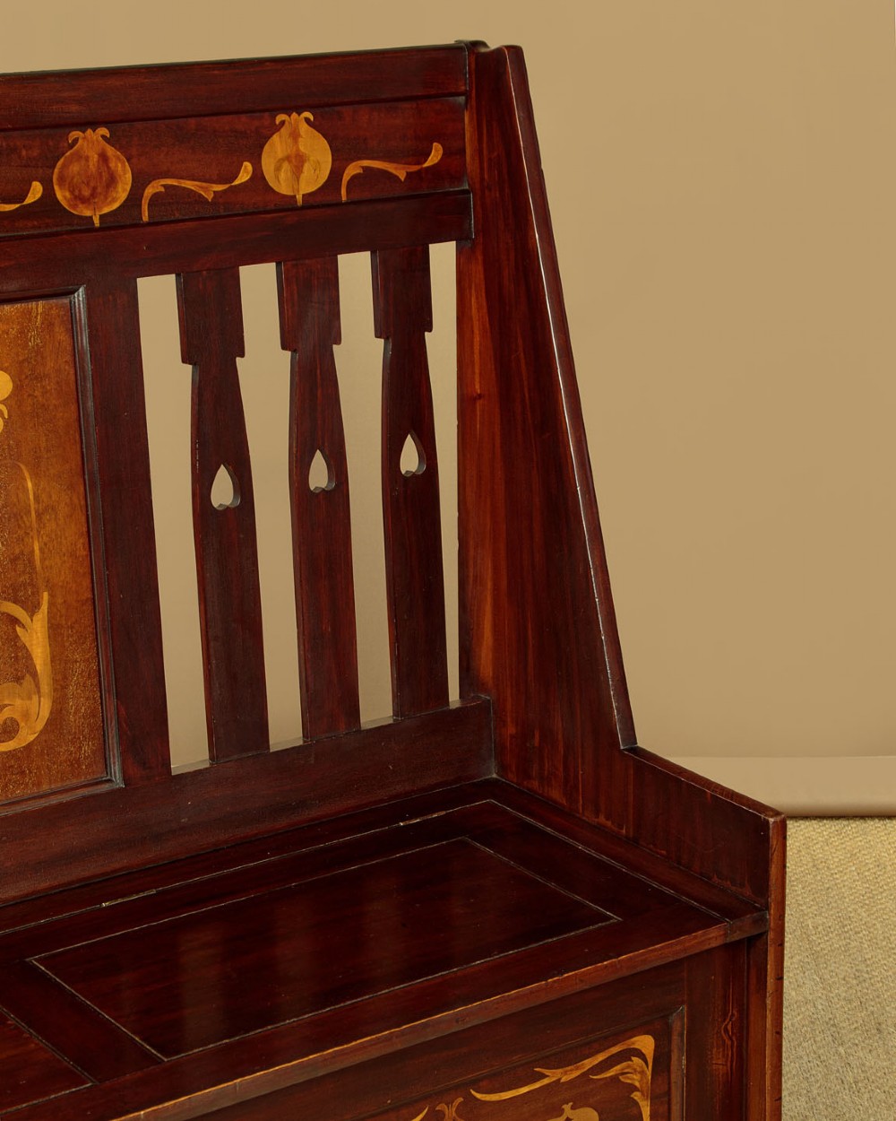 A dark mahogany high-back Arts and Crafts box settle featuring stylised floral marquetry inlay and vertical splat details above a hinged lift-up storage seat. View V