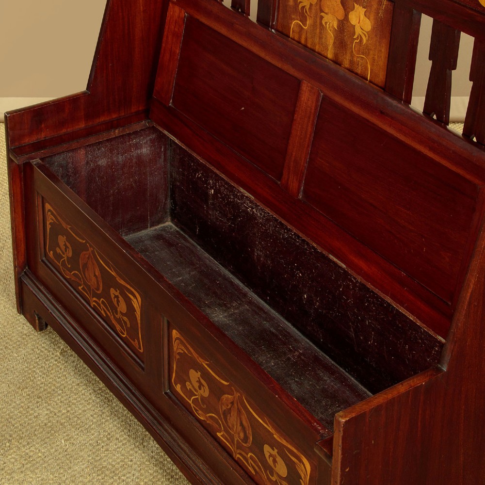 A dark mahogany high-back Arts and Crafts box settle featuring stylised floral marquetry inlay and vertical splat details above a hinged lift-up storage seat. View VIII