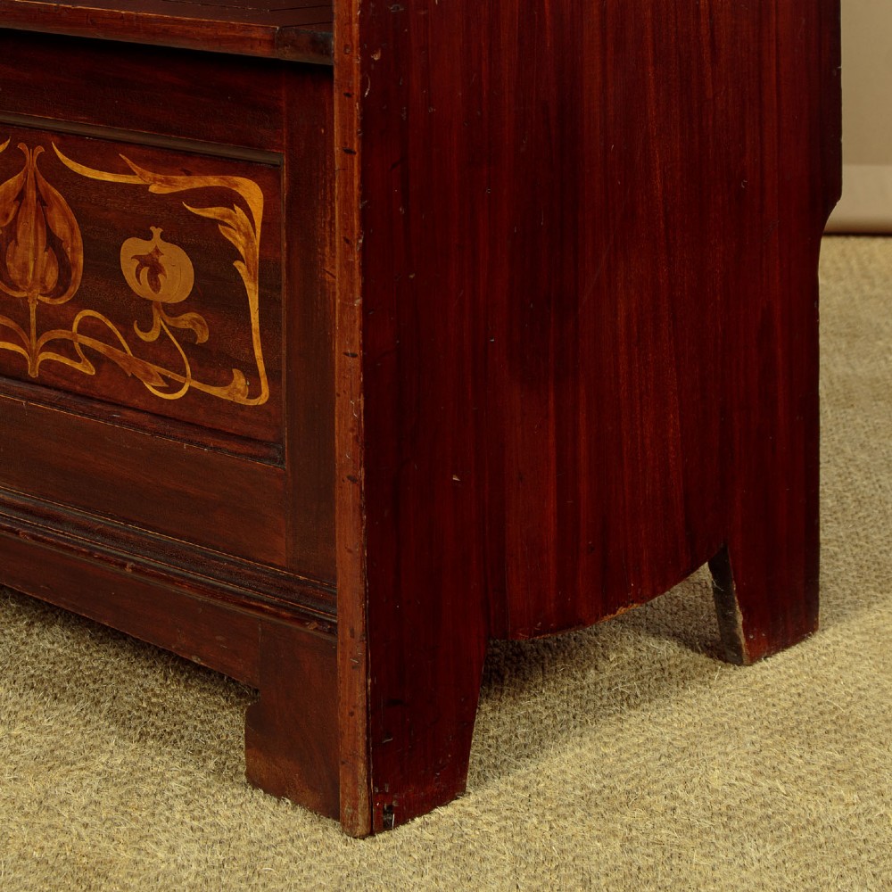 A dark mahogany high-back Arts and Crafts box settle featuring stylised floral marquetry inlay and vertical splat details above a hinged lift-up storage seat. View X