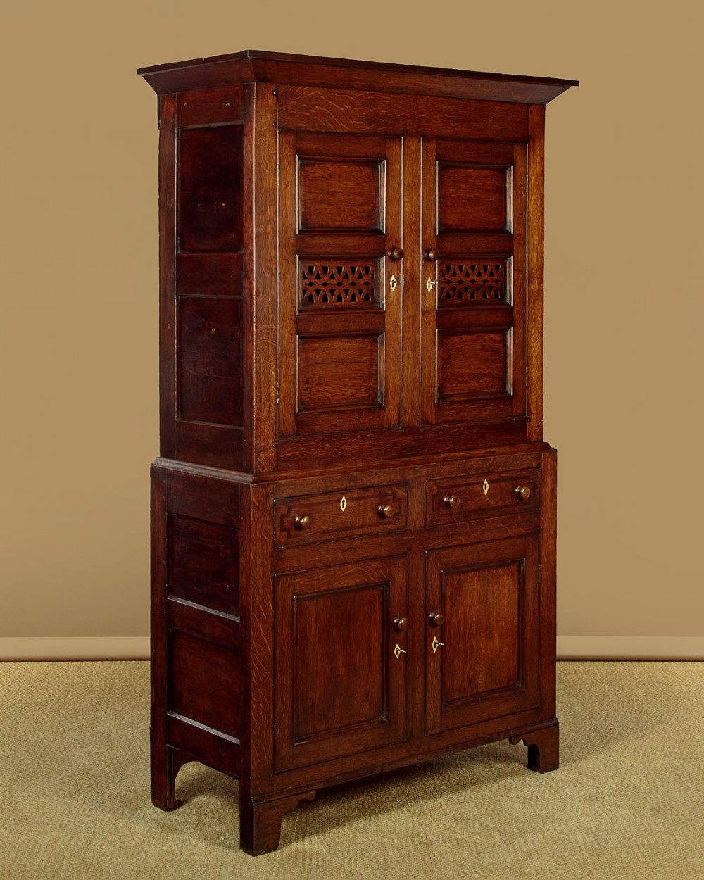 A two-section Georgian Welsh dark oak bread and cheese cupboard featuring upper panelled doors with fretwork ventilation grilles, two drawers, and a double-door lower section.