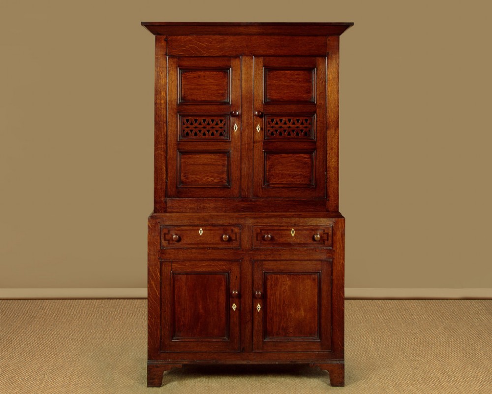 A two-section Georgian Welsh dark oak bread and cheese cupboard featuring upper panelled doors with fretwork ventilation grilles, two drawers, and a double-door lower section. View III