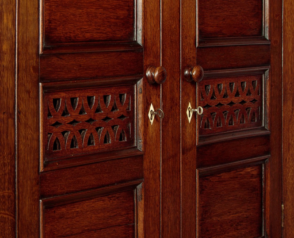 A two-section Georgian Welsh dark oak bread and cheese cupboard featuring upper panelled doors with fretwork ventilation grilles, two drawers, and a double-door lower section. View VII