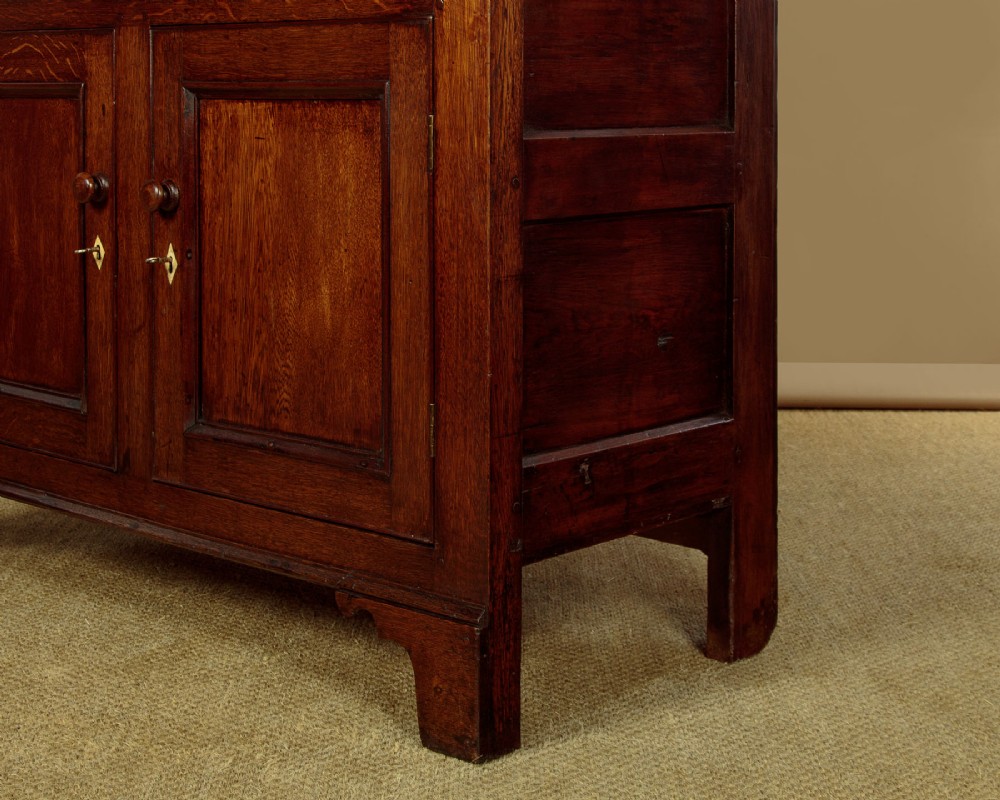 A two-section Georgian Welsh dark oak bread and cheese cupboard featuring upper panelled doors with fretwork ventilation grilles, two drawers, and a double-door lower section. View X