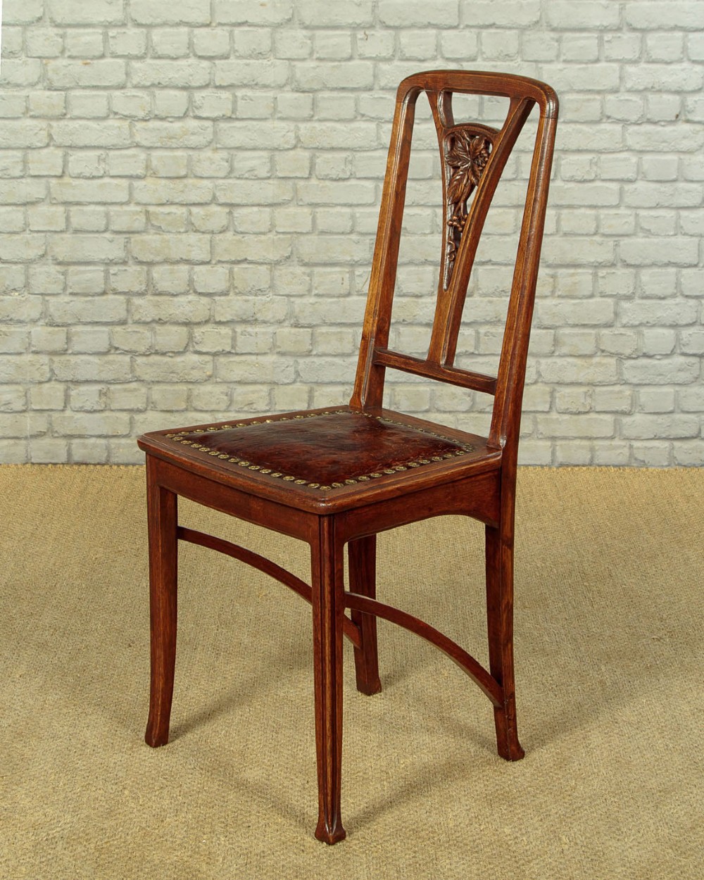 A set of six Art Nouveau oak dining chairs featuring carved botanical backrests and dark brown leather seats with brass stud trim. View III