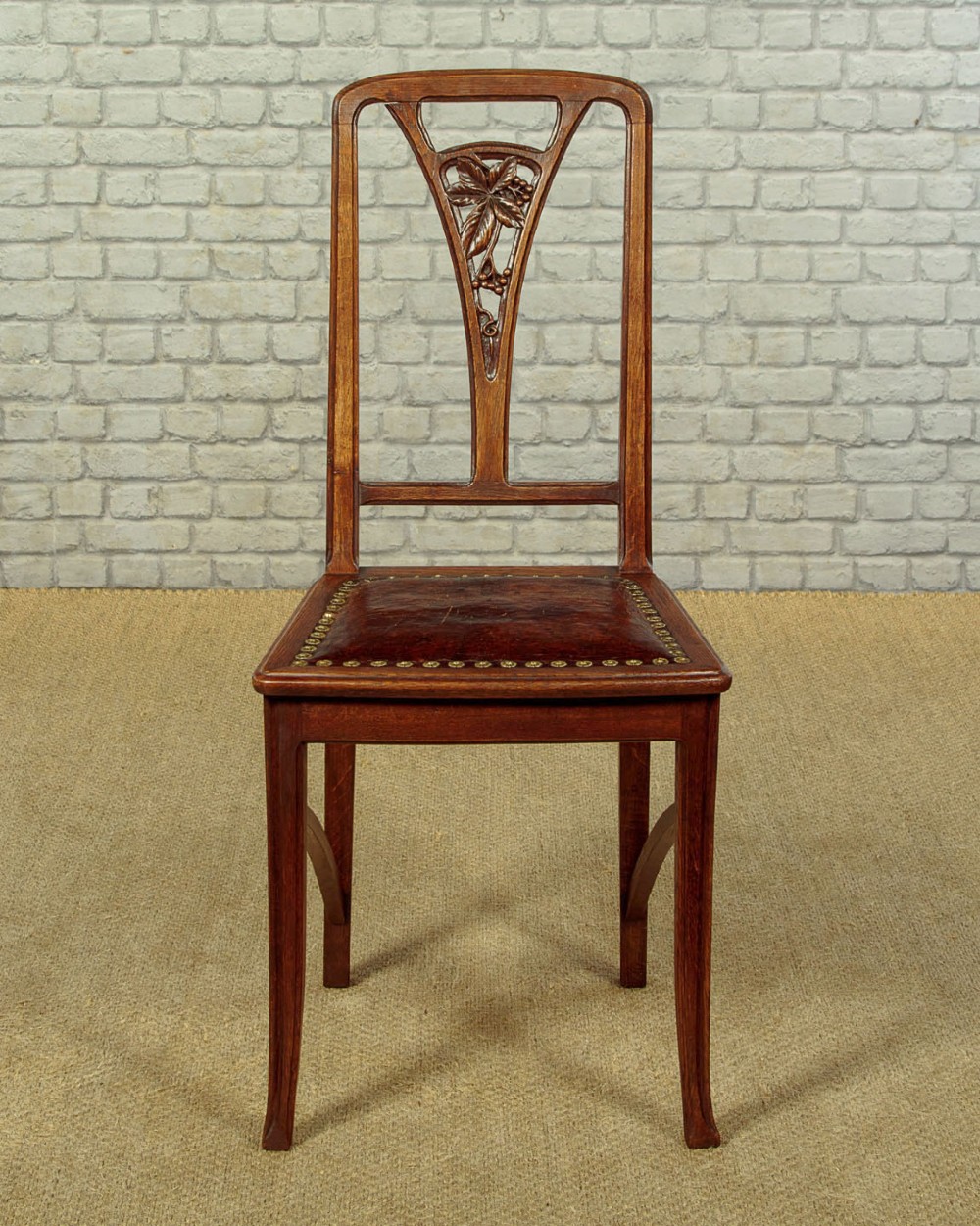 A set of six Art Nouveau oak dining chairs featuring carved botanical backrests and dark brown leather seats with brass stud trim. View IV