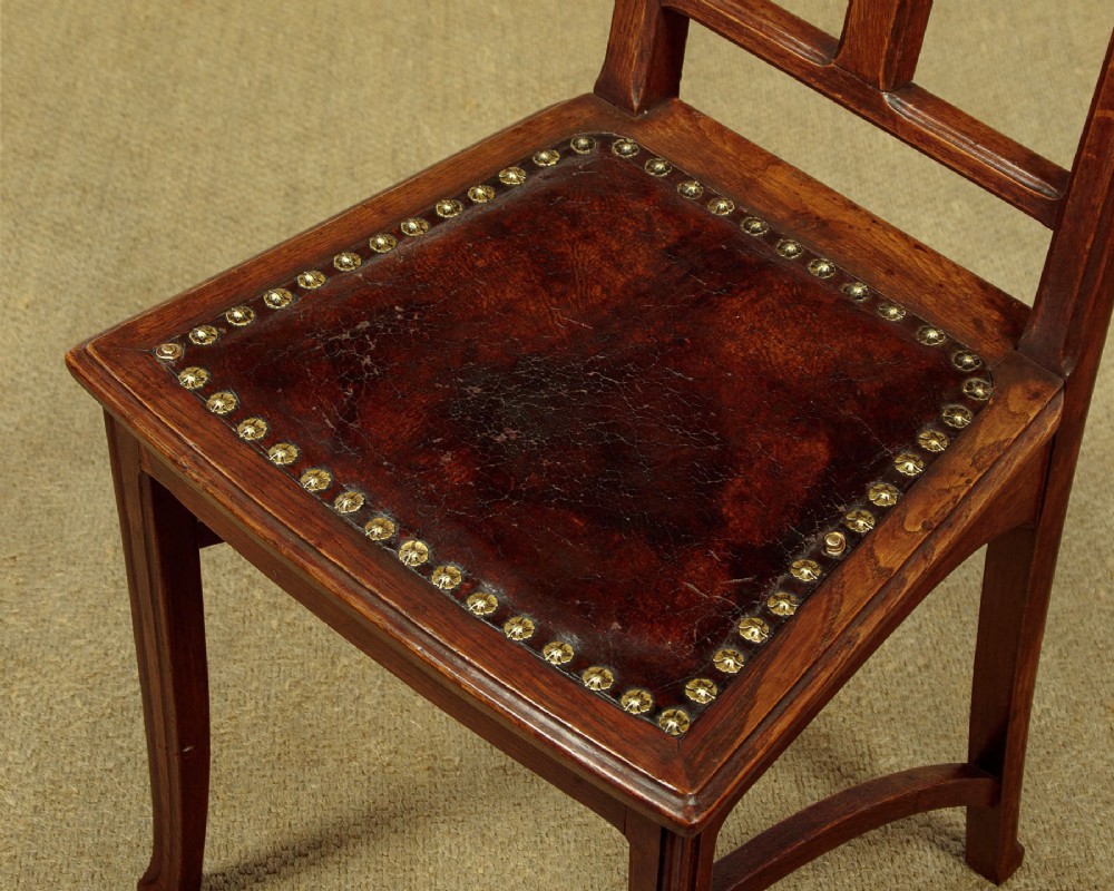 A set of six Art Nouveau oak dining chairs featuring carved botanical backrests and dark brown leather seats with brass stud trim. View VIII