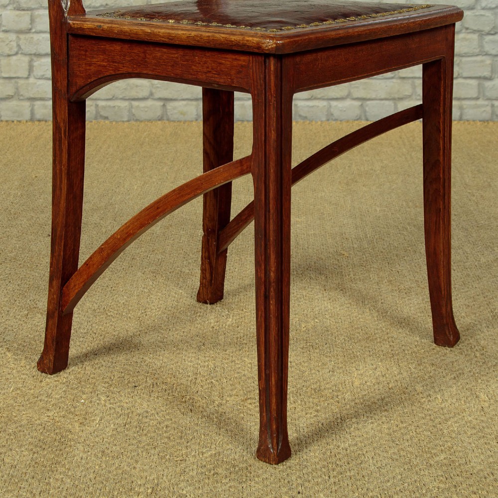 A set of six Art Nouveau oak dining chairs featuring carved botanical backrests and dark brown leather seats with brass stud trim. View XI