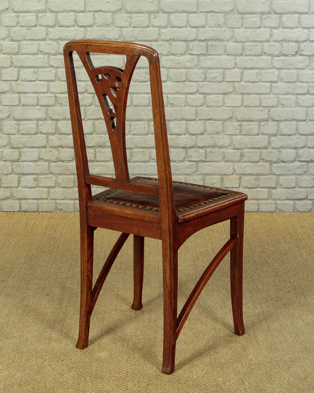 A set of six Art Nouveau oak dining chairs featuring carved botanical backrests and dark brown leather seats with brass stud trim. View XIII