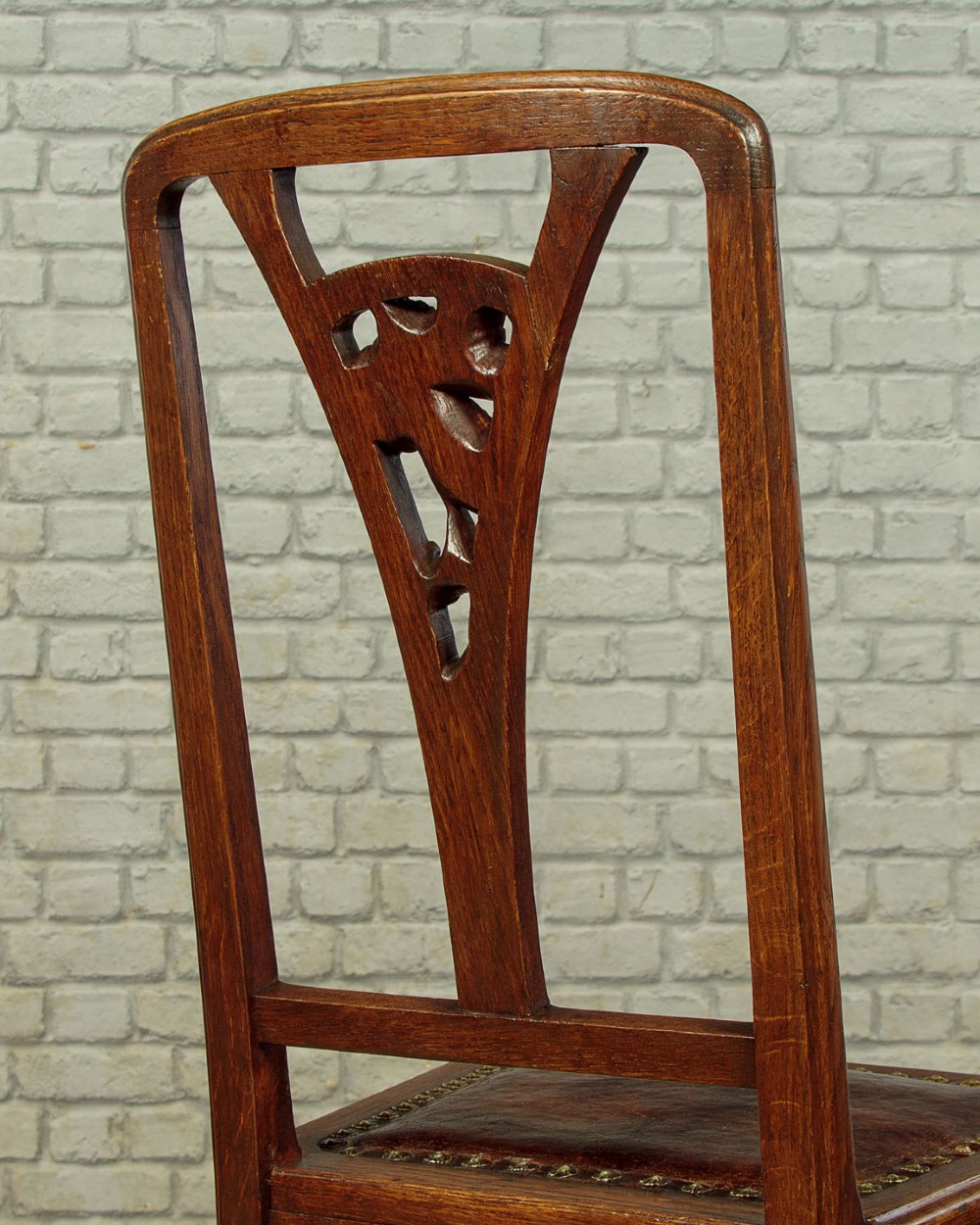 A set of six Art Nouveau oak dining chairs featuring carved botanical backrests and dark brown leather seats with brass stud trim. View XIV