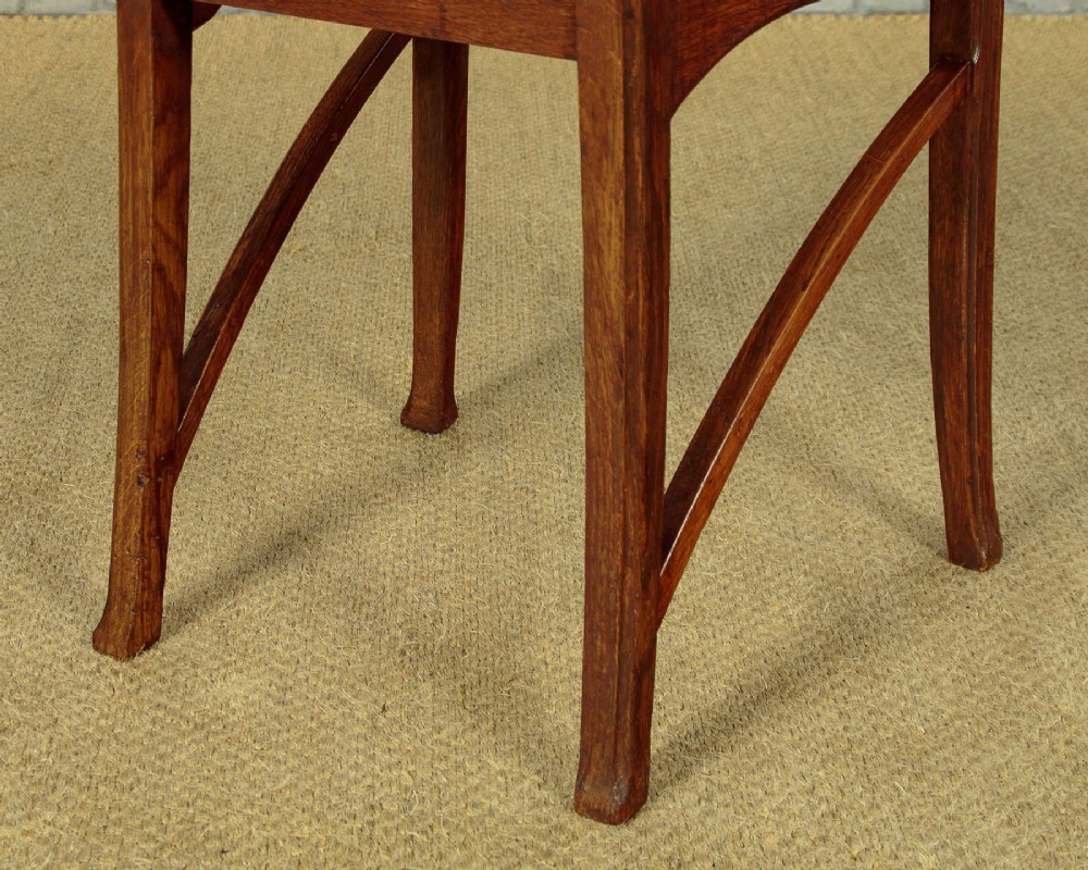 A set of six Art Nouveau oak dining chairs featuring carved botanical backrests and dark brown leather seats with brass stud trim. View XV