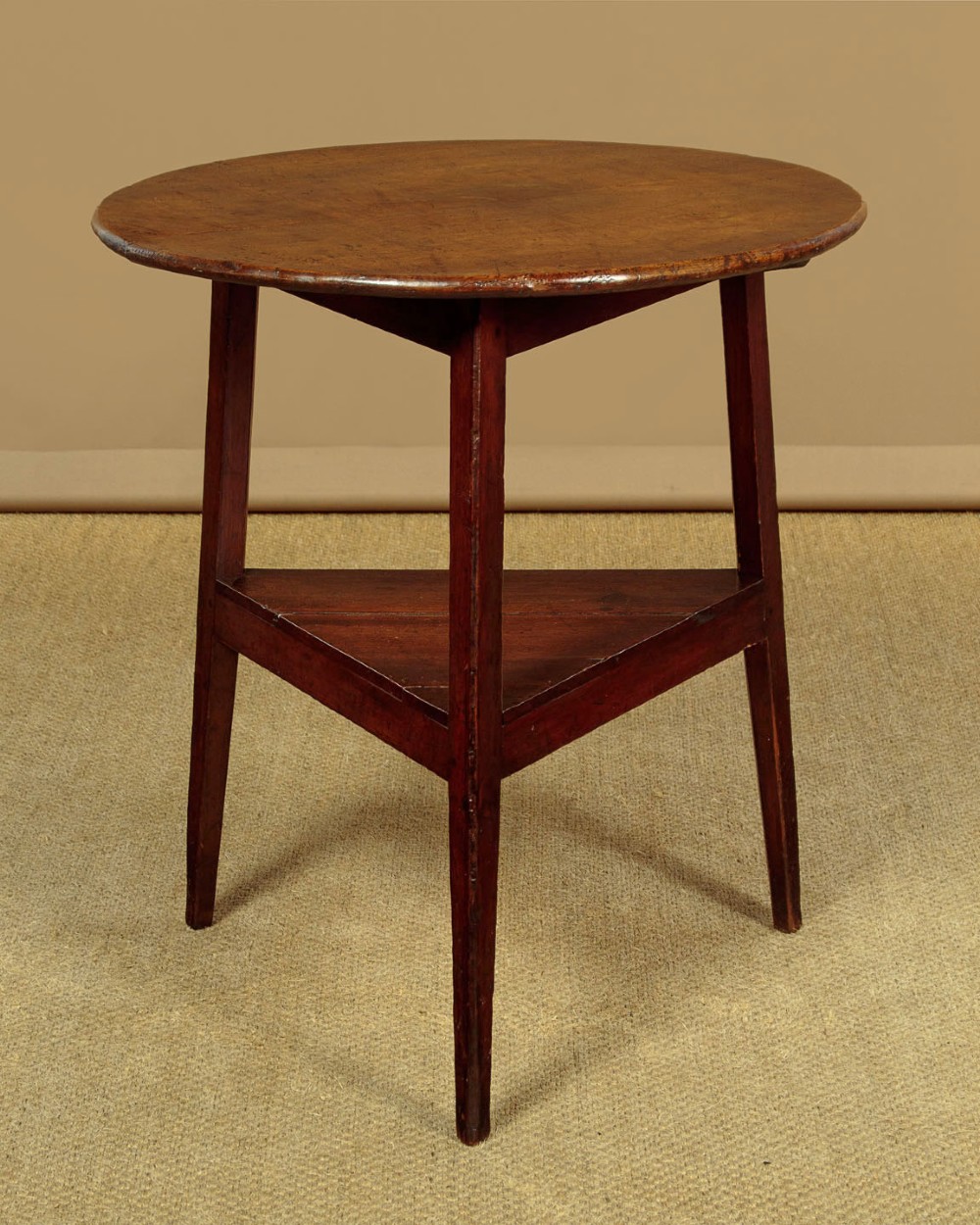 A mid-19th-century pollard oak cricket table with a round top, three splayed legs, and a triangular lower shelf.