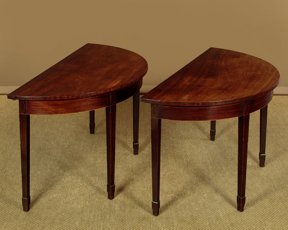 A pair of late George III mahogany demi-lune side tables featuring inlaid aprons and square tapered legs.