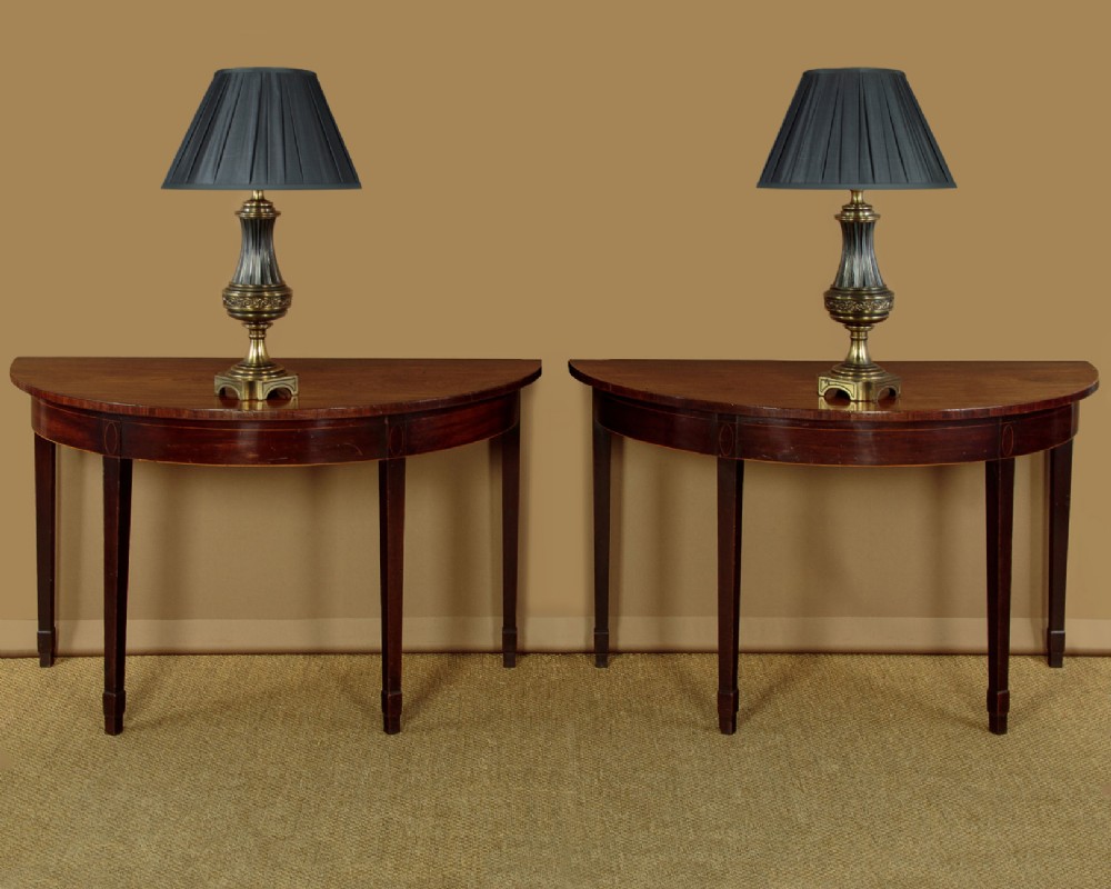 A pair of late George III mahogany demi-lune side tables featuring inlaid aprons and square tapered legs. View II