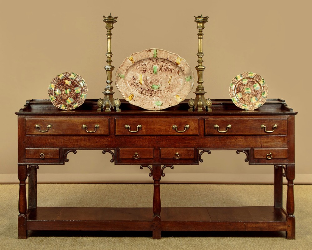 A George III dark oak potboard dresser base featuring three upper drawers, four frieze drawers, brass handles, shaped spandrels, and a low open shelf. View II