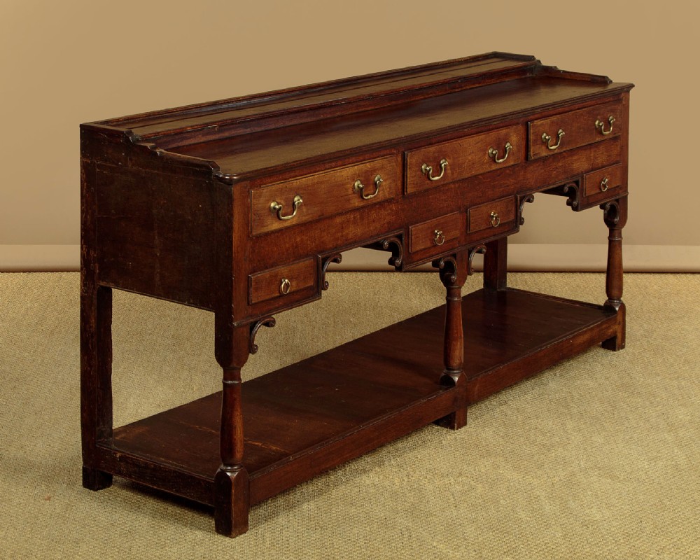 A George III dark oak potboard dresser base featuring three upper drawers, four frieze drawers, brass handles, shaped spandrels, and a low open shelf. View III