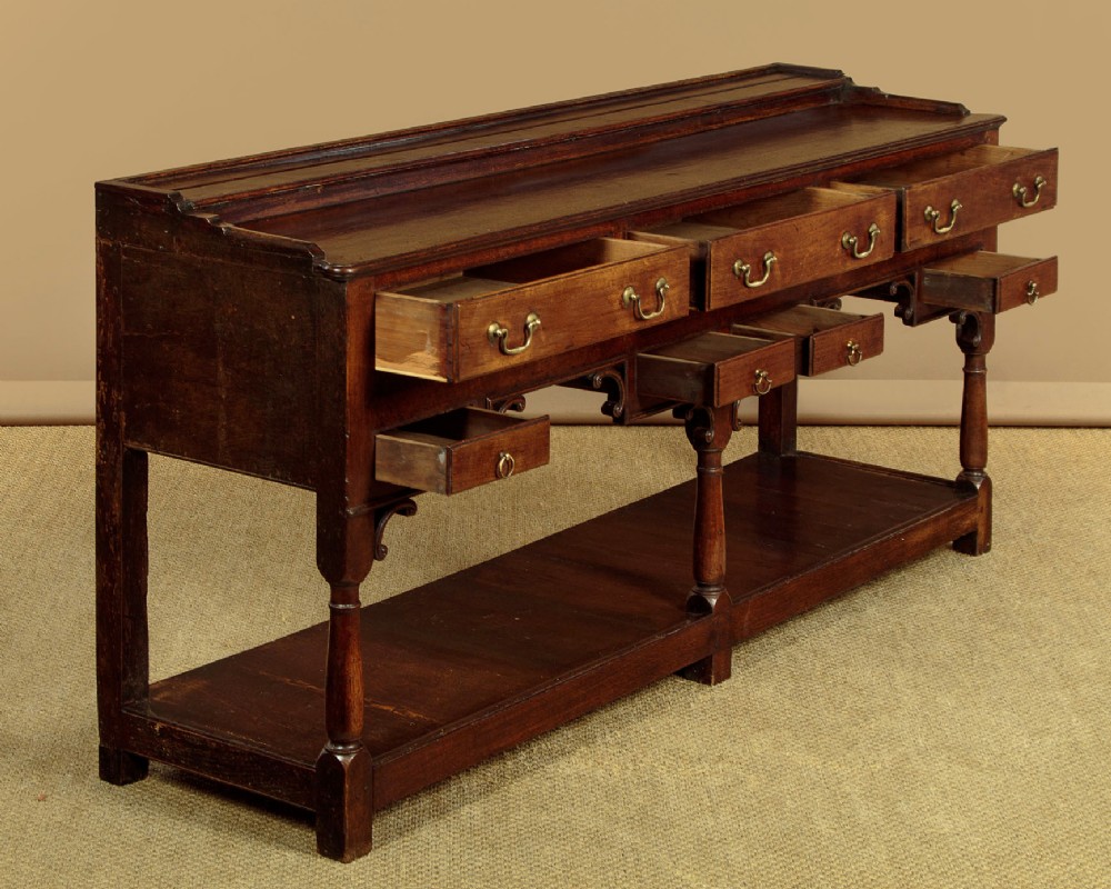A George III dark oak potboard dresser base featuring three upper drawers, four frieze drawers, brass handles, shaped spandrels, and a low open shelf. View V