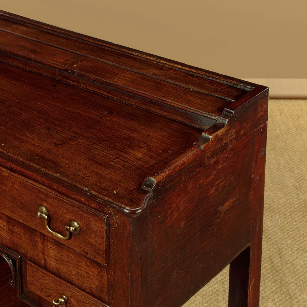 A George III dark oak potboard dresser base featuring three upper drawers, four frieze drawers, brass handles, shaped spandrels, and a low open shelf. View VII