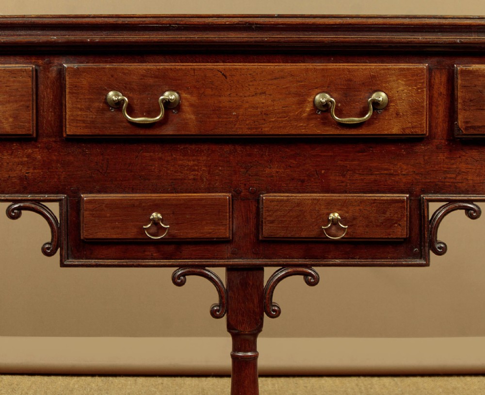 A George III dark oak potboard dresser base featuring three upper drawers, four frieze drawers, brass handles, shaped spandrels, and a low open shelf. View VIII