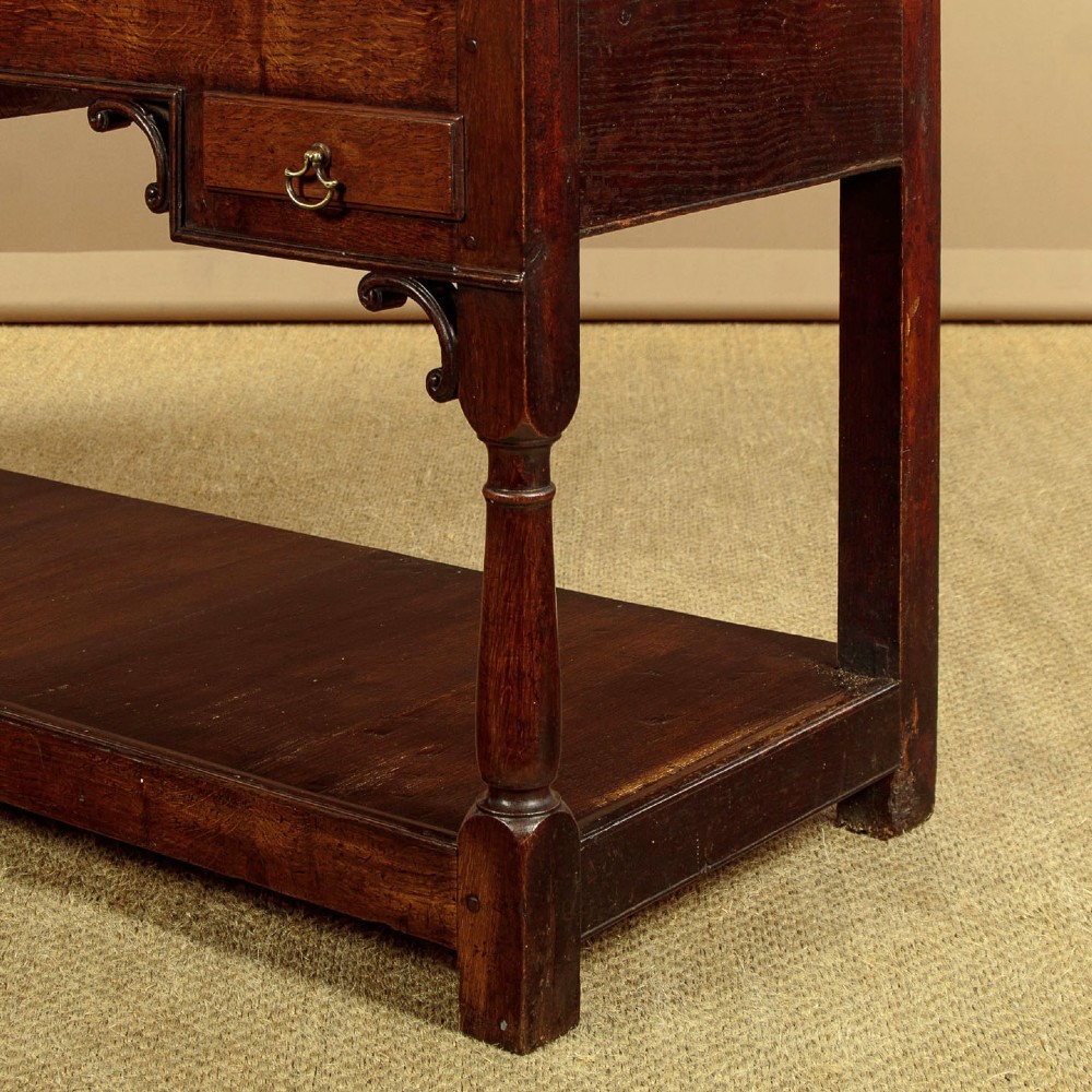A George III dark oak potboard dresser base featuring three upper drawers, four frieze drawers, brass handles, shaped spandrels, and a low open shelf. View XIII