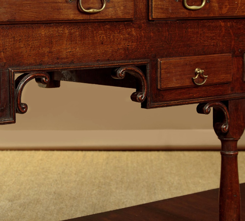 A George III dark oak potboard dresser base featuring three upper drawers, four frieze drawers, brass handles, shaped spandrels, and a low open shelf. View XIV