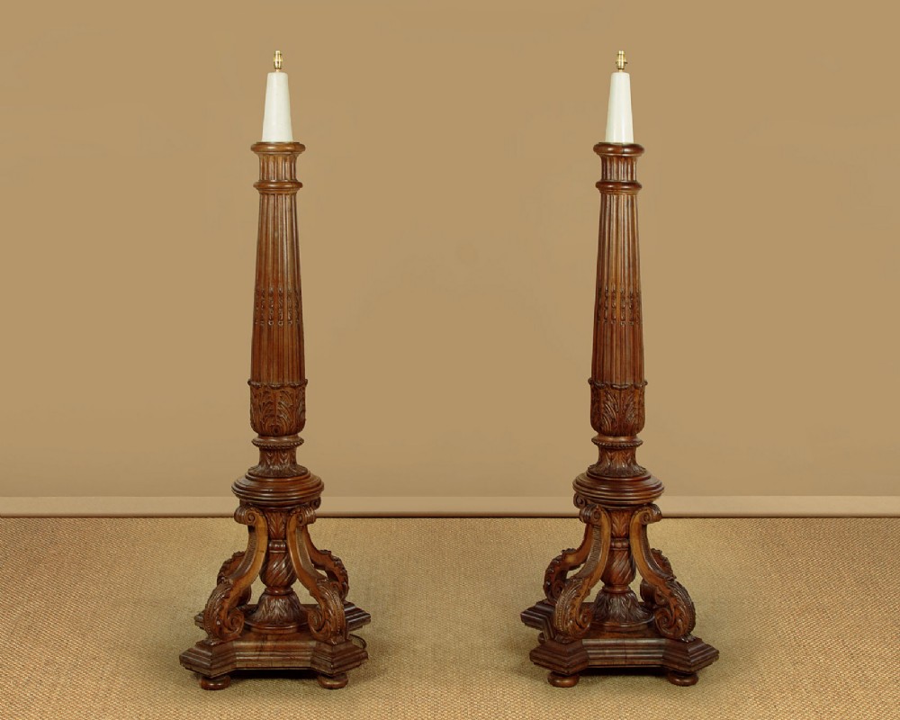 A pair of carved walnut standard lamps featuring fluted tapered shafts, acanthus scroll bases, and candle-style bulb sockets.