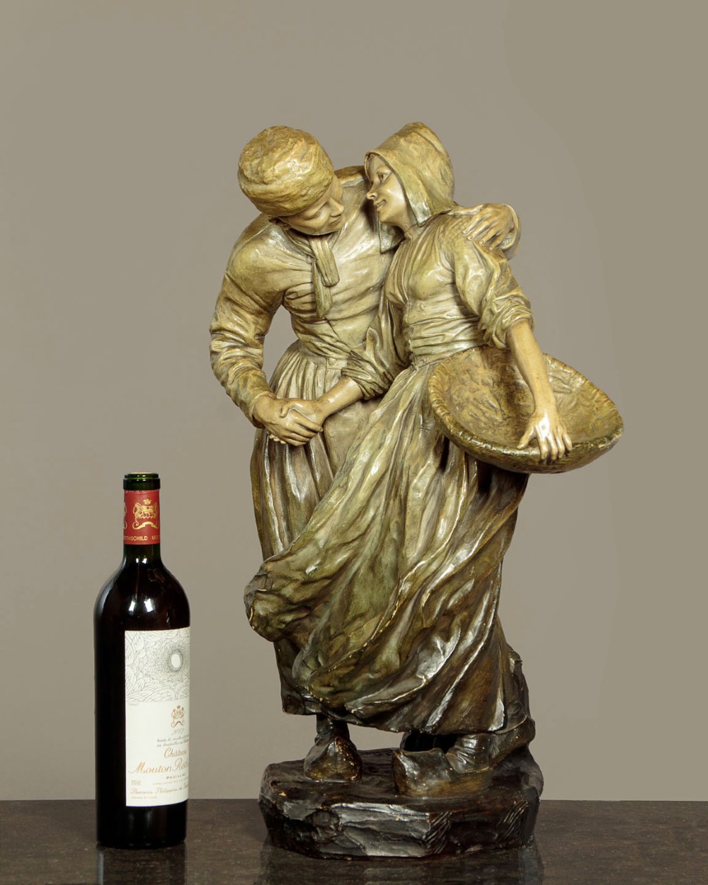 A patinated terracotta sculpture depicting a man and woman in traditional rural attire embracing while holding a woven basket. View II