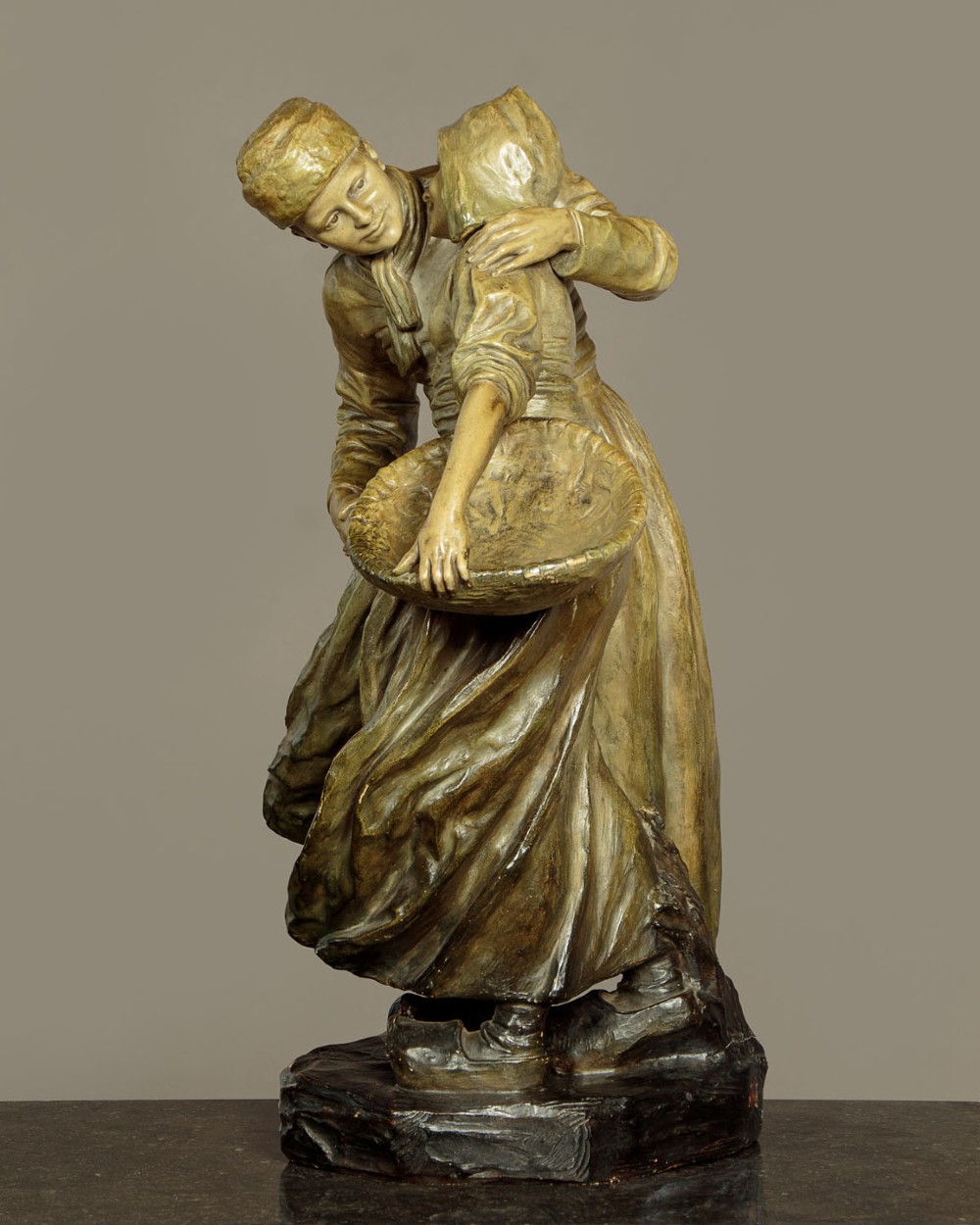 A patinated terracotta sculpture depicting a man and woman in traditional rural attire embracing while holding a woven basket. View III
