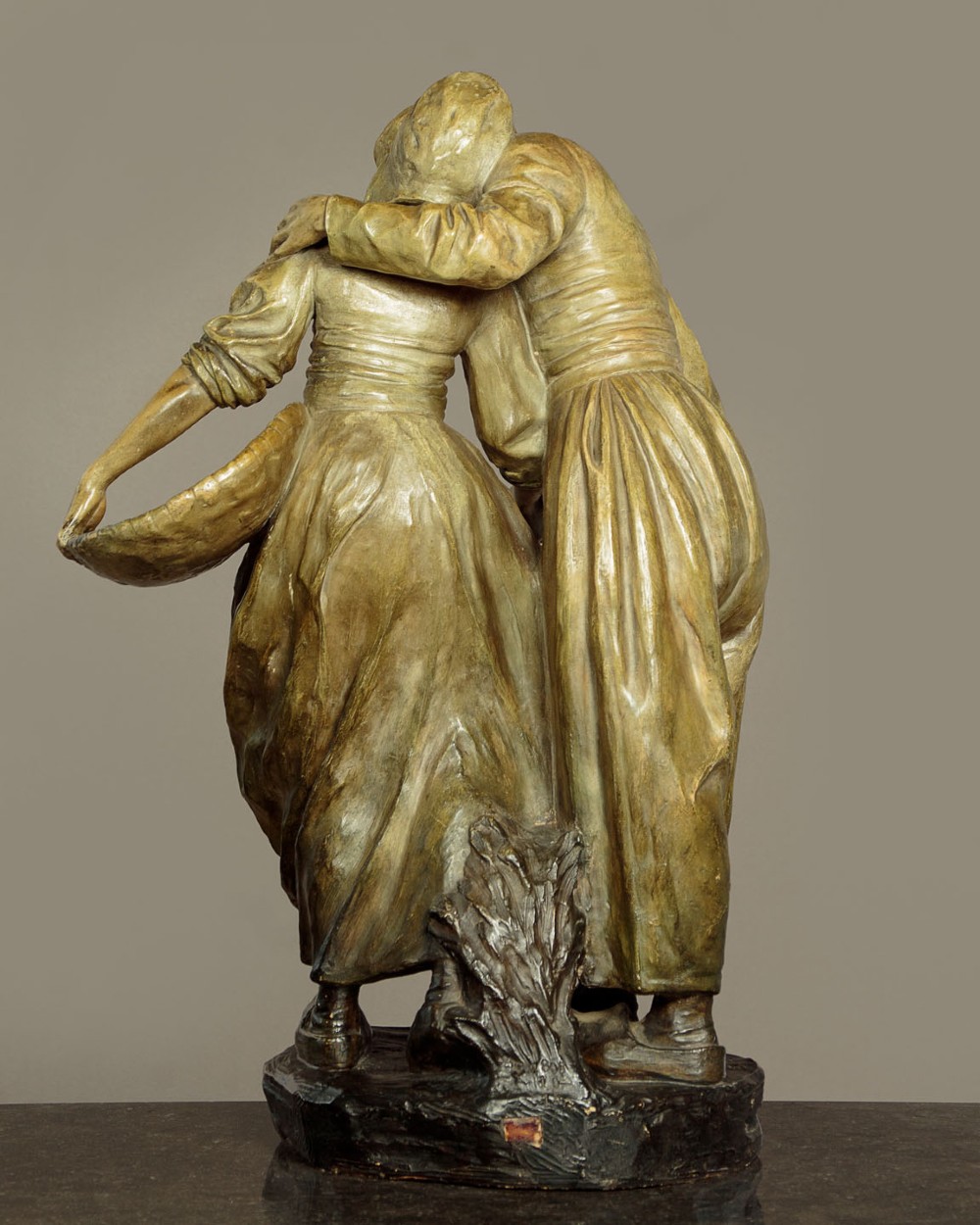 A patinated terracotta sculpture depicting a man and woman in traditional rural attire embracing while holding a woven basket. View IV