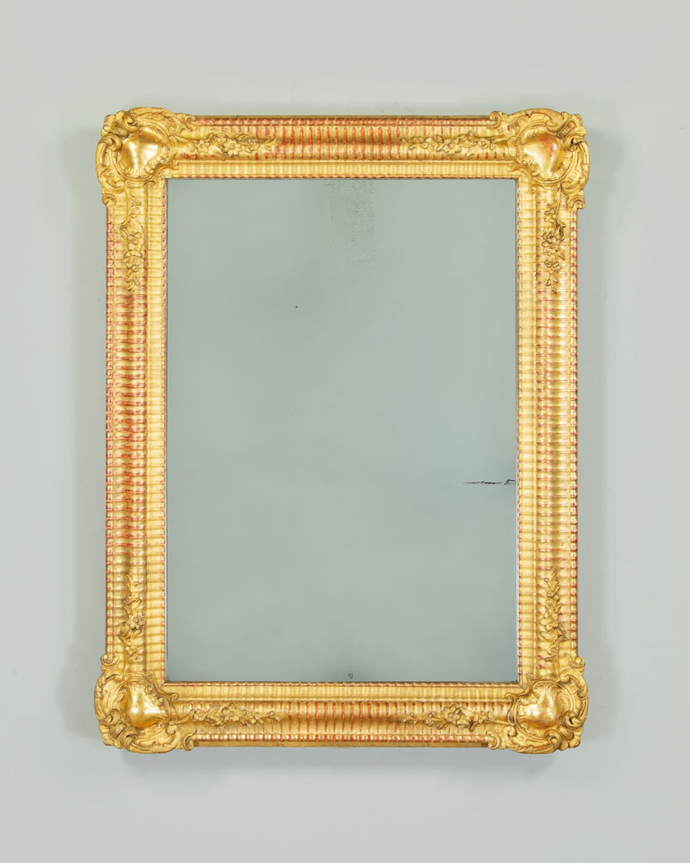 A late 19th-century rectangular French giltwood wall mirror featuring carved corner cartouches, gadrooned borders, and visible red bole beneath gold leaf.