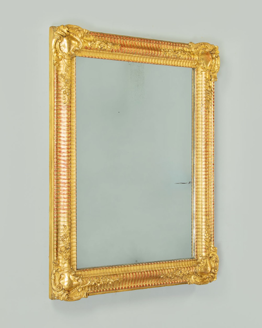 A late 19th-century rectangular French giltwood wall mirror featuring carved corner cartouches, gadrooned borders, and visible red bole beneath gold leaf. View II