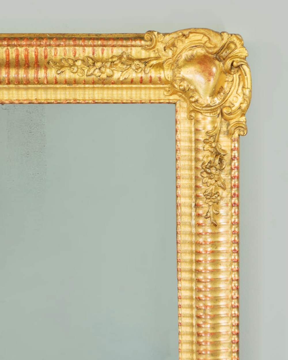 A late 19th-century rectangular French giltwood wall mirror featuring carved corner cartouches, gadrooned borders, and visible red bole beneath gold leaf. View IV