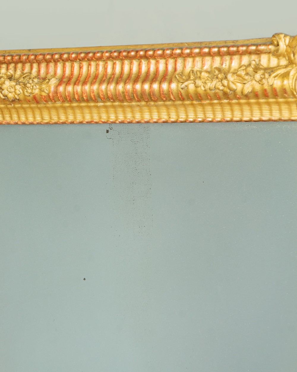 A late 19th-century rectangular French giltwood wall mirror featuring carved corner cartouches, gadrooned borders, and visible red bole beneath gold leaf. View V