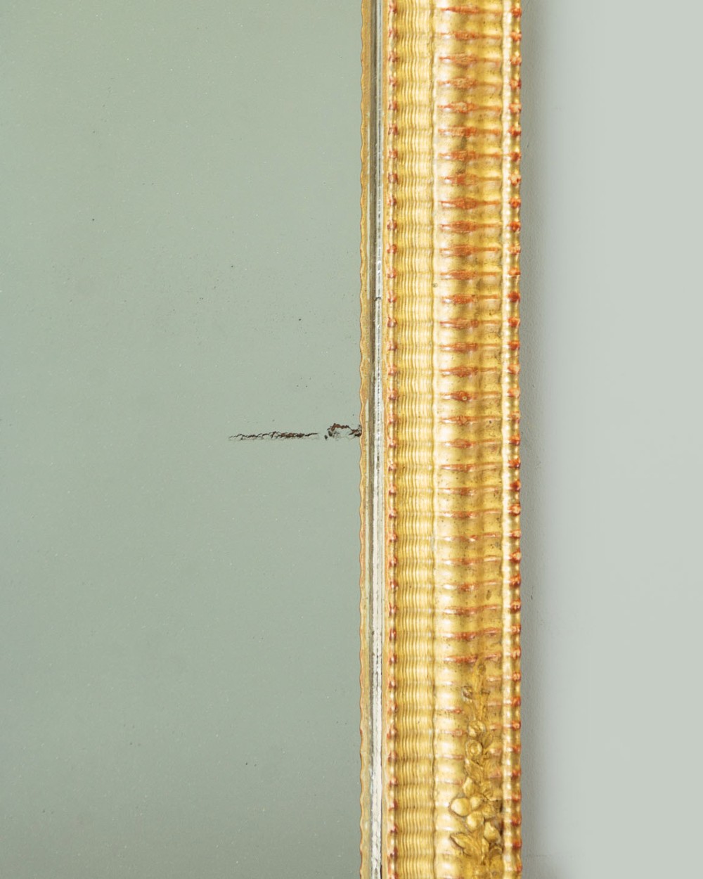 A late 19th-century rectangular French giltwood wall mirror featuring carved corner cartouches, gadrooned borders, and visible red bole beneath gold leaf. View VI