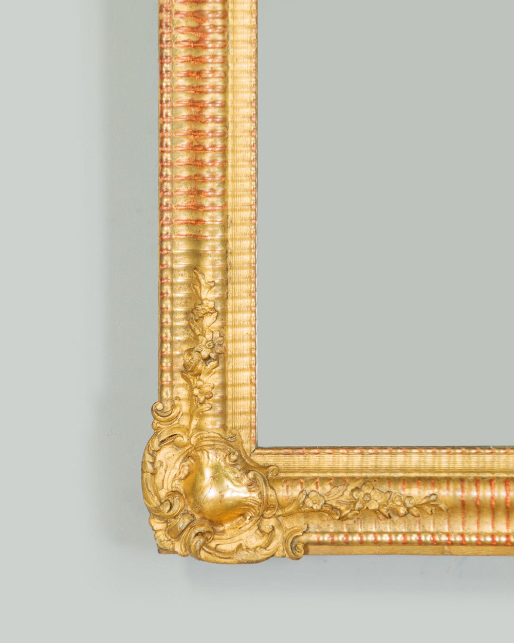 A late 19th-century rectangular French giltwood wall mirror featuring carved corner cartouches, gadrooned borders, and visible red bole beneath gold leaf. View VII