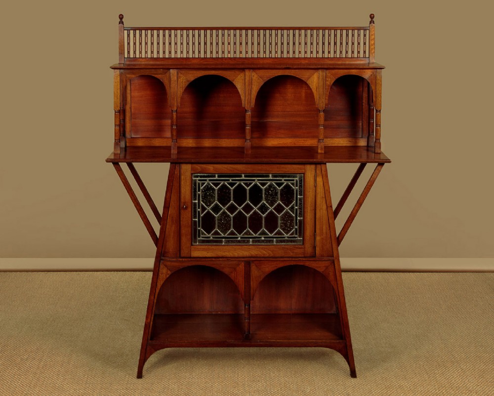 An Arts and Crafts oak side cabinet featuring an upper spindle gallery, arched open shelves, diagonal side struts, and a central cabinet door with leaded glass.
