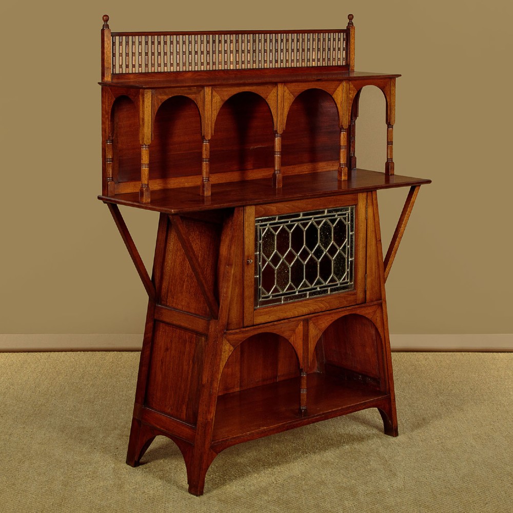 An Arts and Crafts oak side cabinet featuring an upper spindle gallery, arched open shelves, diagonal side struts, and a central cabinet door with leaded glass. View II