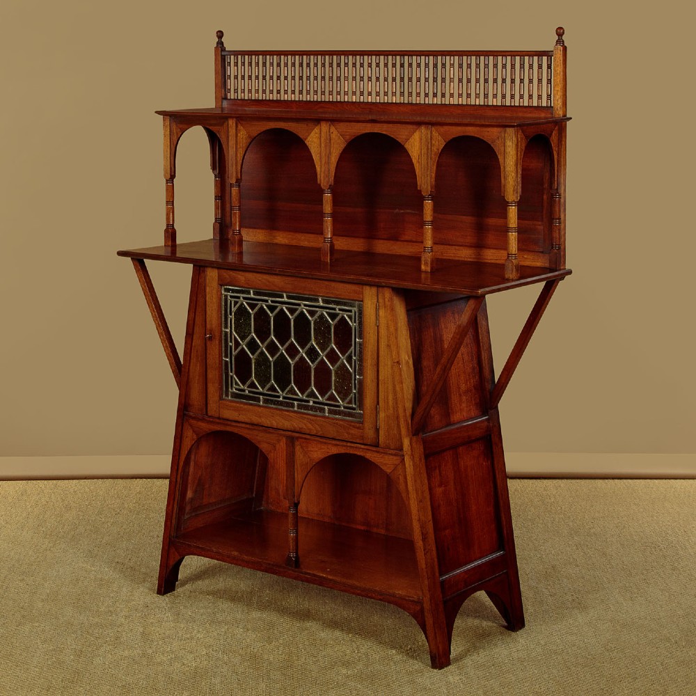An Arts and Crafts oak side cabinet featuring an upper spindle gallery, arched open shelves, diagonal side struts, and a central cabinet door with leaded glass. View III