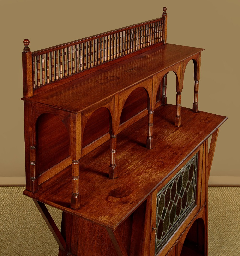 An Arts and Crafts oak side cabinet featuring an upper spindle gallery, arched open shelves, diagonal side struts, and a central cabinet door with leaded glass. View V