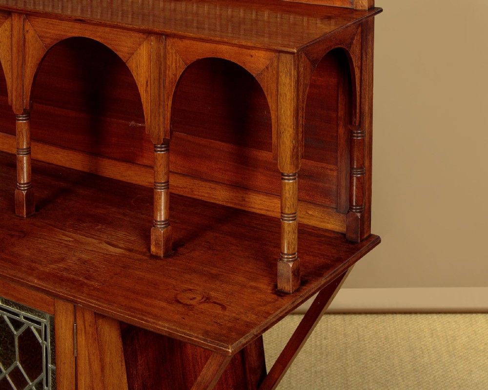 An Arts and Crafts oak side cabinet featuring an upper spindle gallery, arched open shelves, diagonal side struts, and a central cabinet door with leaded glass. View VII