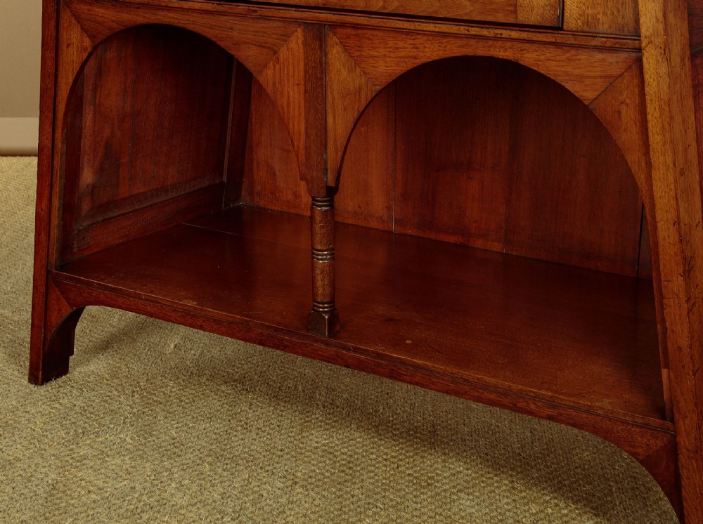 An Arts and Crafts oak side cabinet featuring an upper spindle gallery, arched open shelves, diagonal side struts, and a central cabinet door with leaded glass. View X